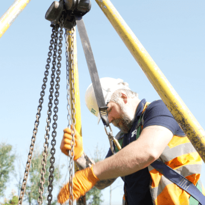 Photograph of a man and a woman in orange high visibility jackets talking and pointing at a piece of white paper in the man's hands, stood in front of a T-T Service Van.