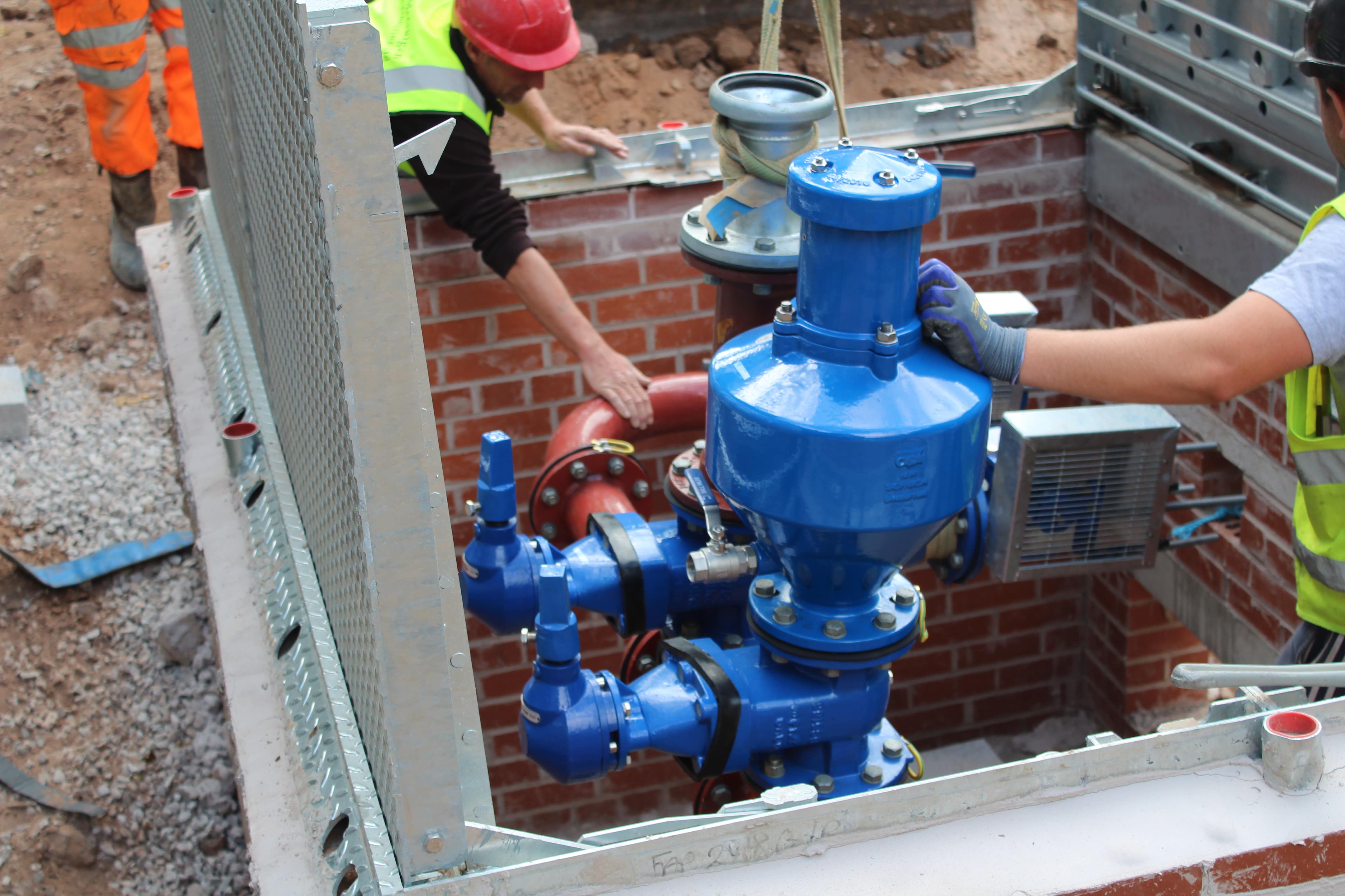Two service engineers installing valves in a pumping station valve chamber.