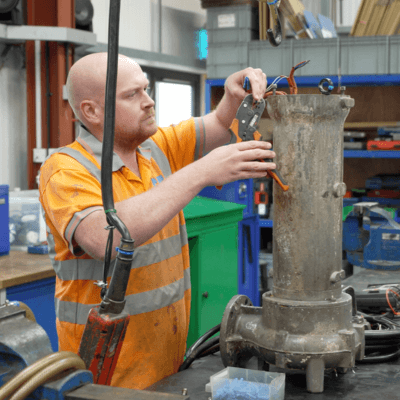 A T-T Repairs engineer repairing a Kino Titan Pump, wearing a yellow high visibility vest and tightening a bolt on the bottom of the pump.